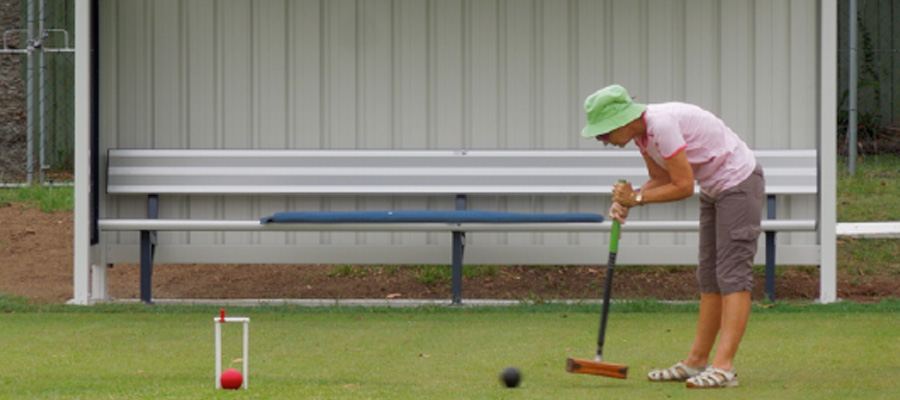 A member in a green hat taking a croquet shot, ball and hoop in the foreground