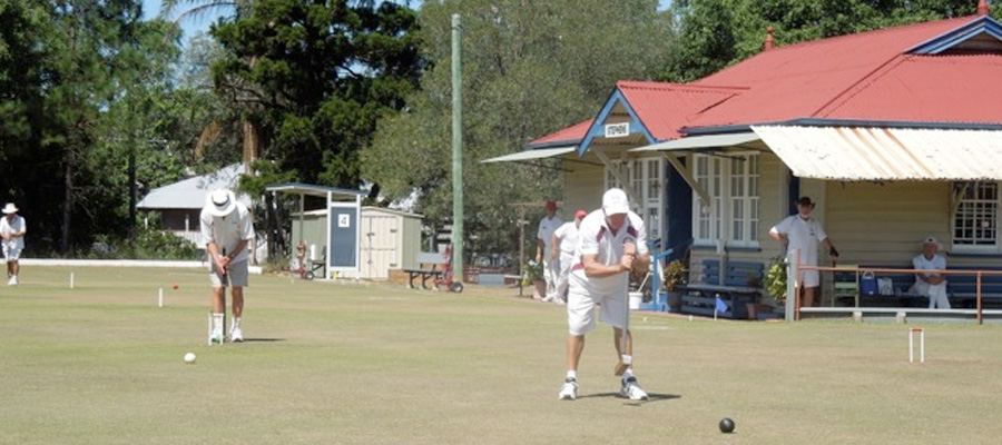 Members playing in front of the red-roofed clubhouse, others watching from the verandah