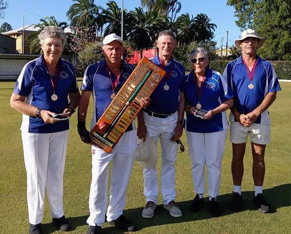 Five croquet players in blue uniforms stand on a lawn, holding a trophy and medals after a competition